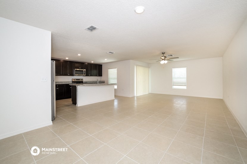 an empty living room with a kitchen and a ceiling fan