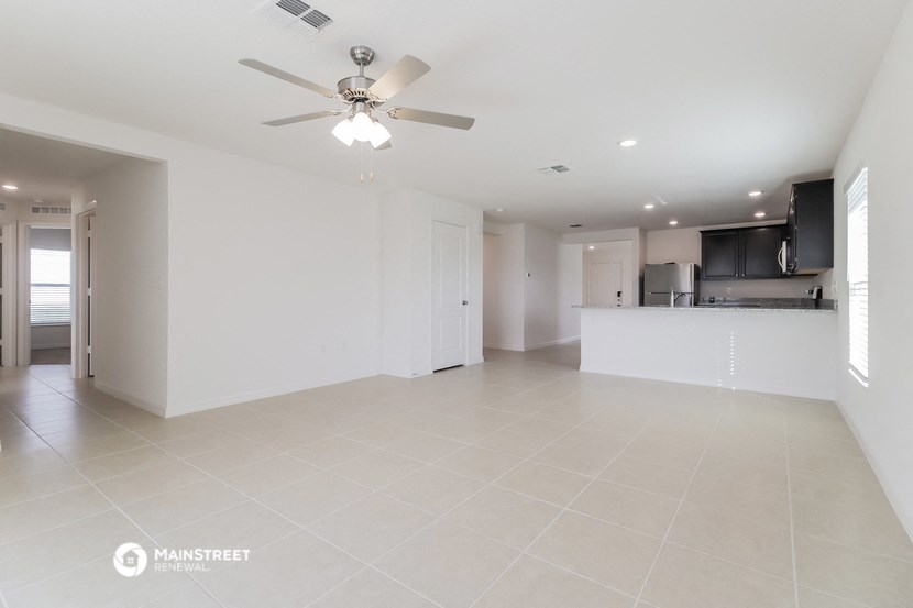 an empty living room with a ceiling fan and a kitchen