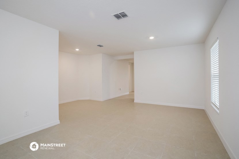 the spacious living room with white walls and tile flooring