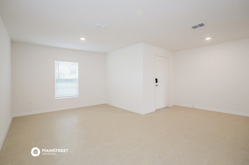 the spacious living room with white walls and tile floors