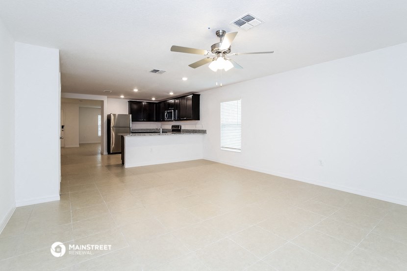 an empty living room and kitchen with a ceiling fan