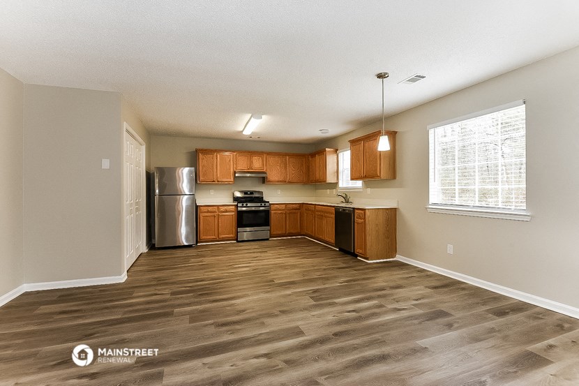 an empty kitchen with wooden floors and a stainless steel refrigerator