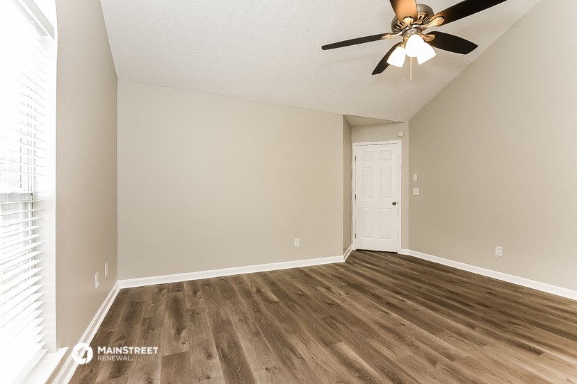 an empty living room with a ceiling fan and a door