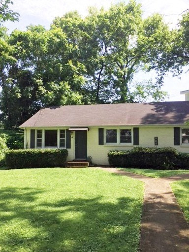 a small yellow house with a yard and trees