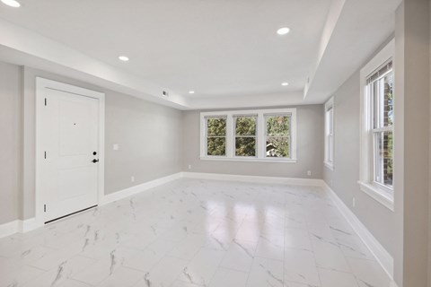A spacious room with white marble flooring and a large window.