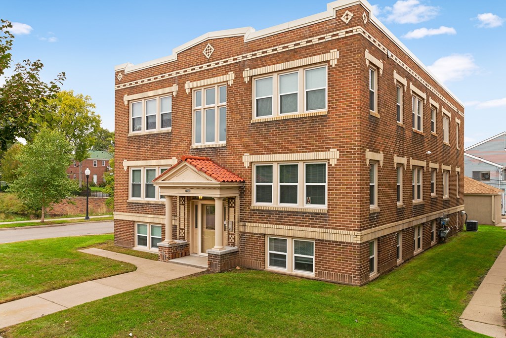a red brick apartment building with a green lawn and a sidewalk