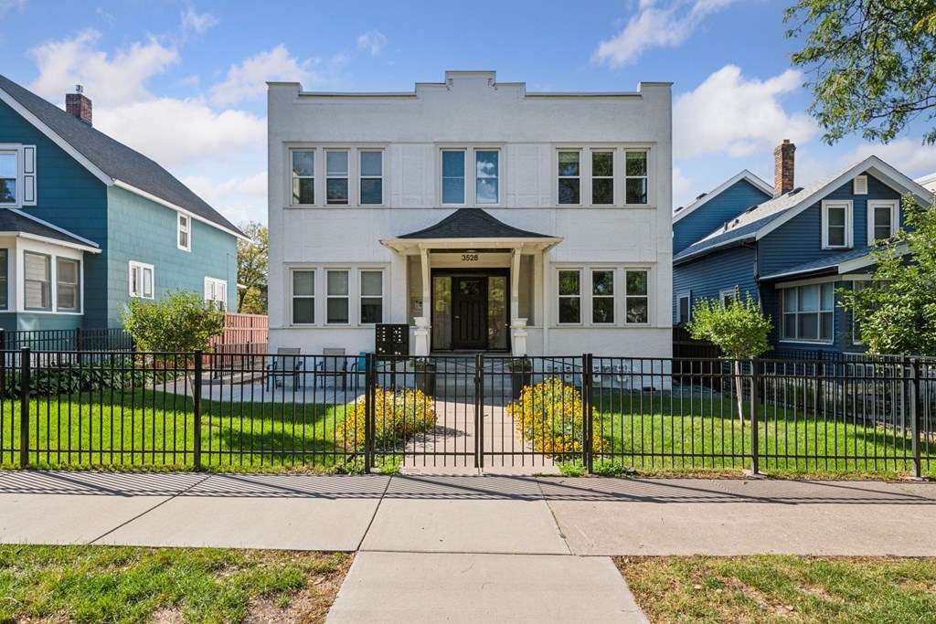 A white two-story house with a black fence in front.