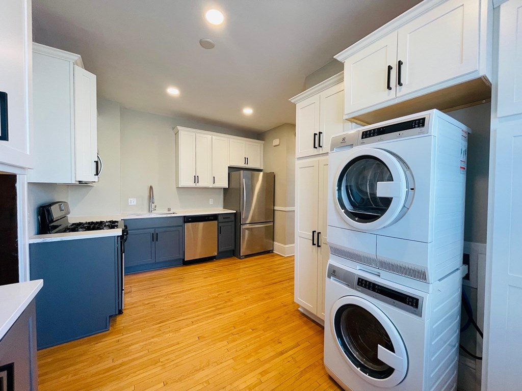 A white washing machine is in a kitchen with wooden floors.