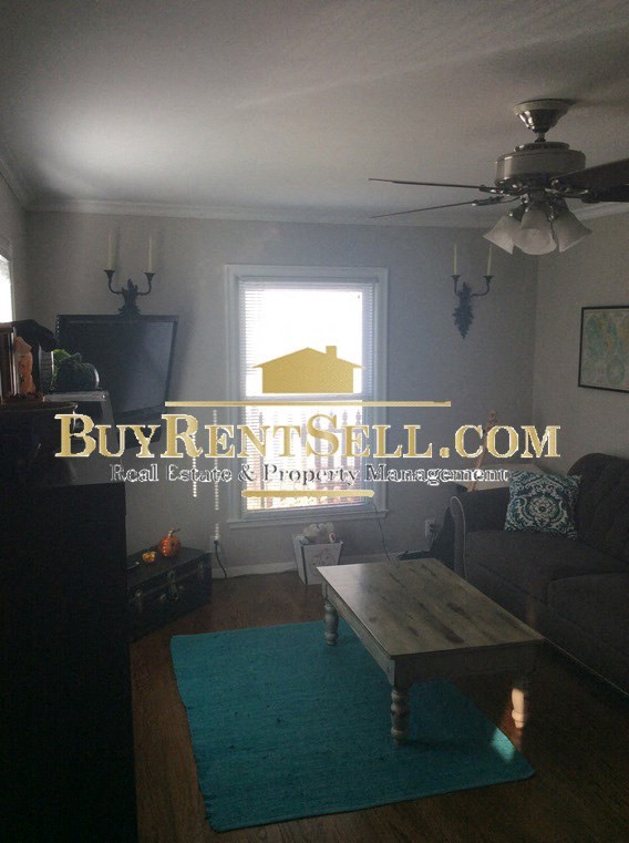 A living room with a BuyRentBelow.com logo on the wall.