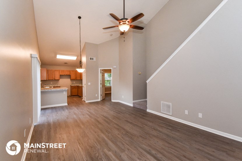 an empty living room with a ceiling fan and a kitchen