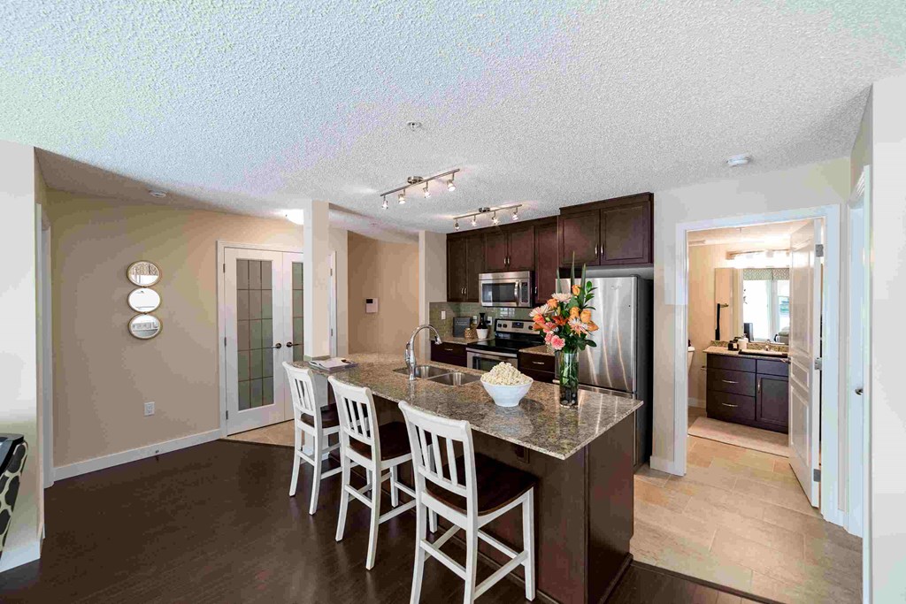 a kitchen with a granite counter top island with white chairs
