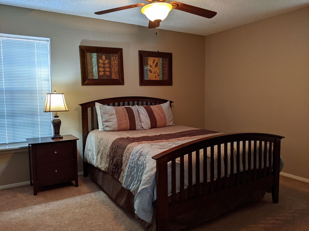 A bedroom with a bed, nightstand, and two pictures on the wall.