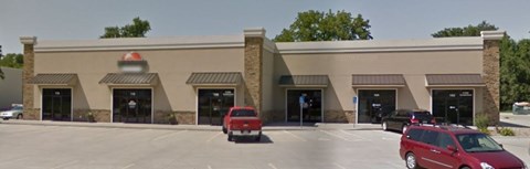 A red car is parked in front of a building with a red logo on it.
