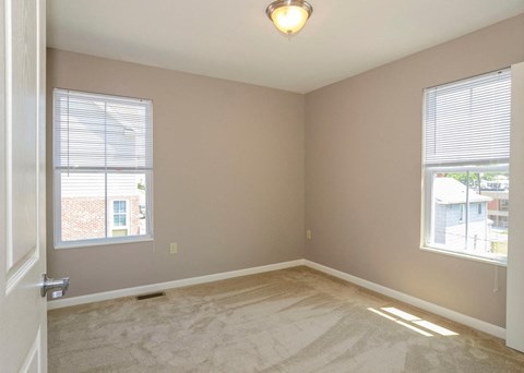 an empty bedroom with two windows and a carpeted floor