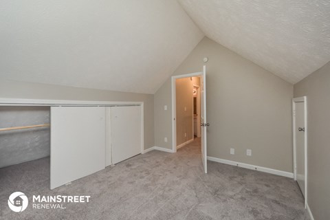 the living room of an apartment with carpet and a door to the hallway