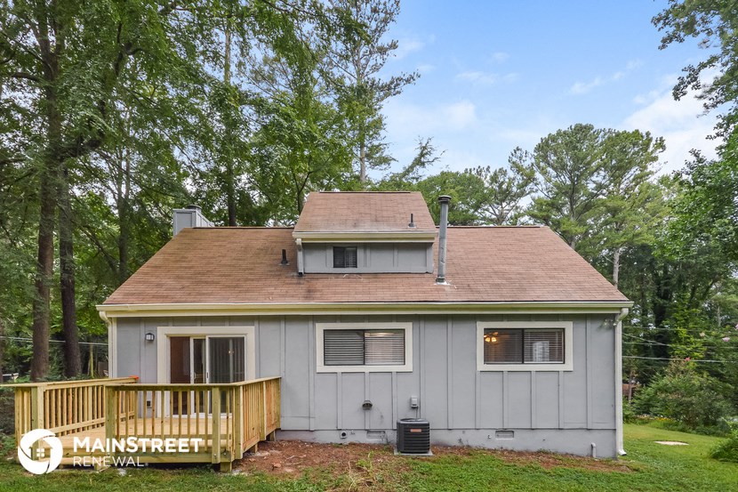 a small gray house with a deck and trees