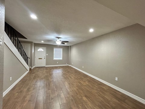 A spacious room with wooden flooring and a staircase.