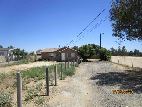 A dirt road leads to a house with a fence on the right side.