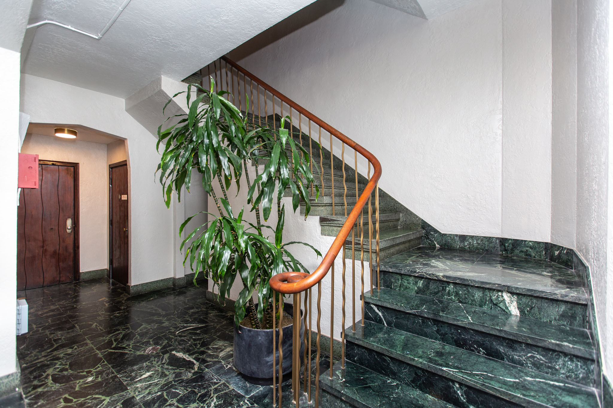 A plant sits on a stand next to a staircase.