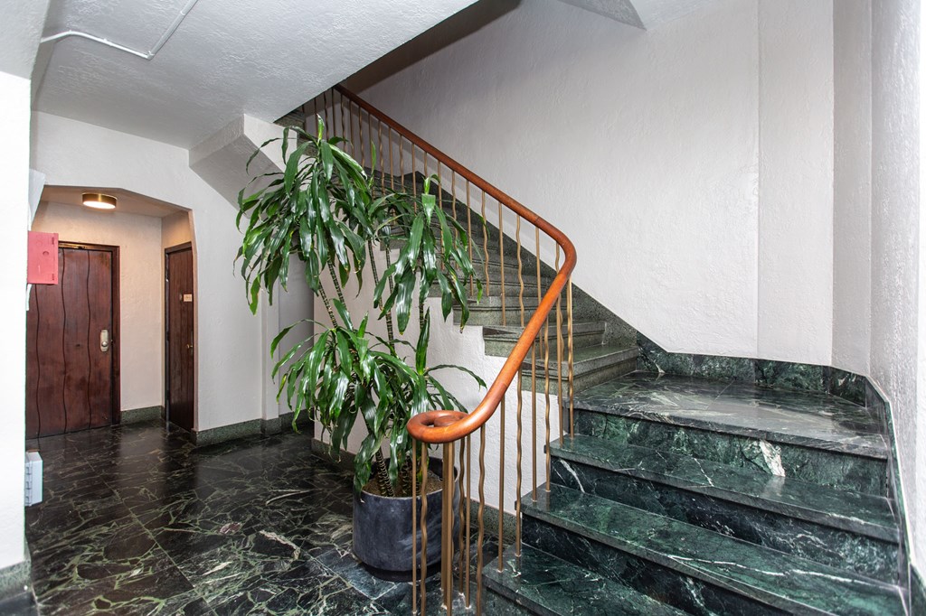 A plant sits on a stand next to a staircase.