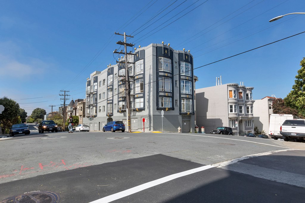 A street view of a residential area with apartment buildings and cars parked on the side of the road.
