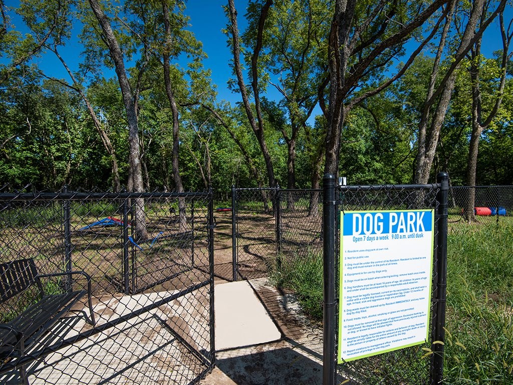 a dog park sign in front of a fence and trees