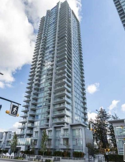A tall, modern glass building stands under a partly cloudy sky.