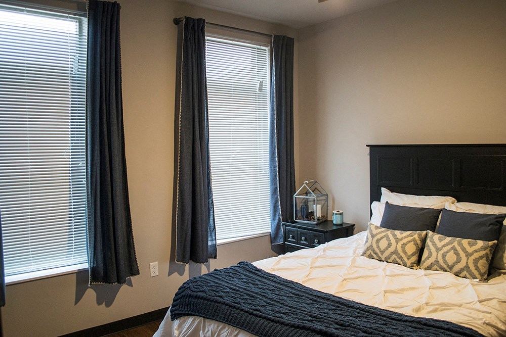 a bedroom with a bed and two windows with black curtains