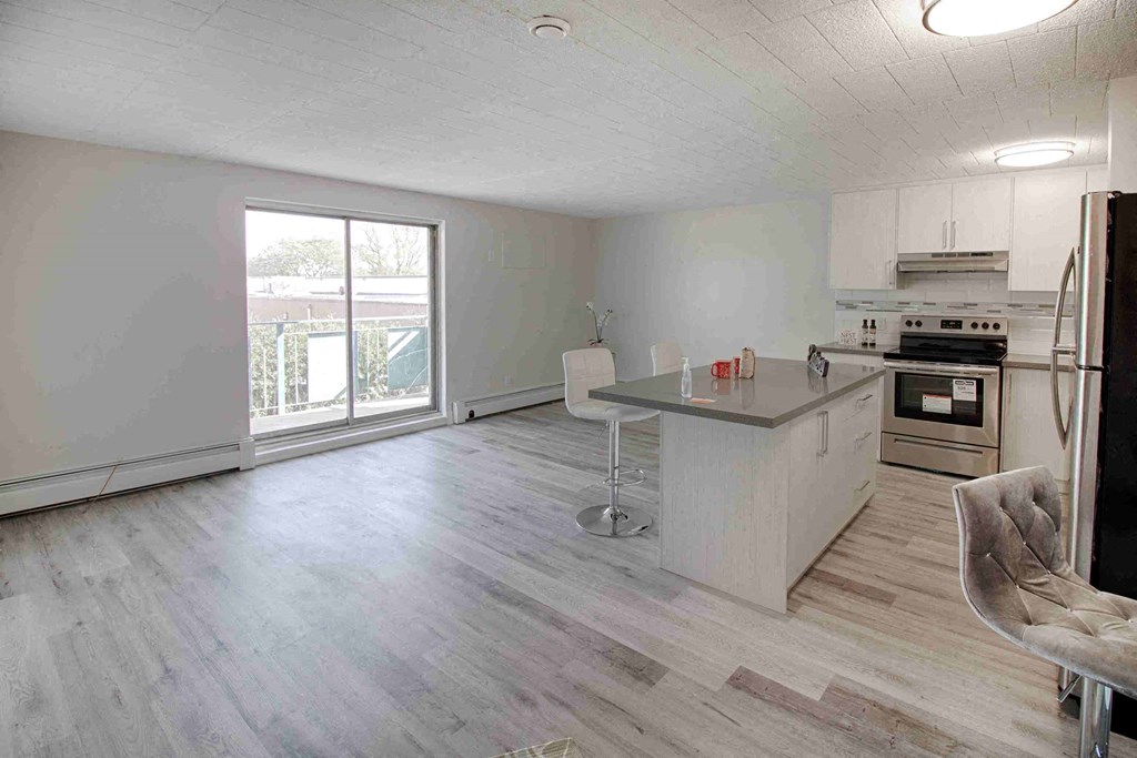 an empty living room with a kitchen and a large window