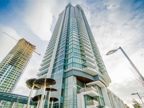 A modern skyscraper with a glass facade stands tall against a partly cloudy sky.