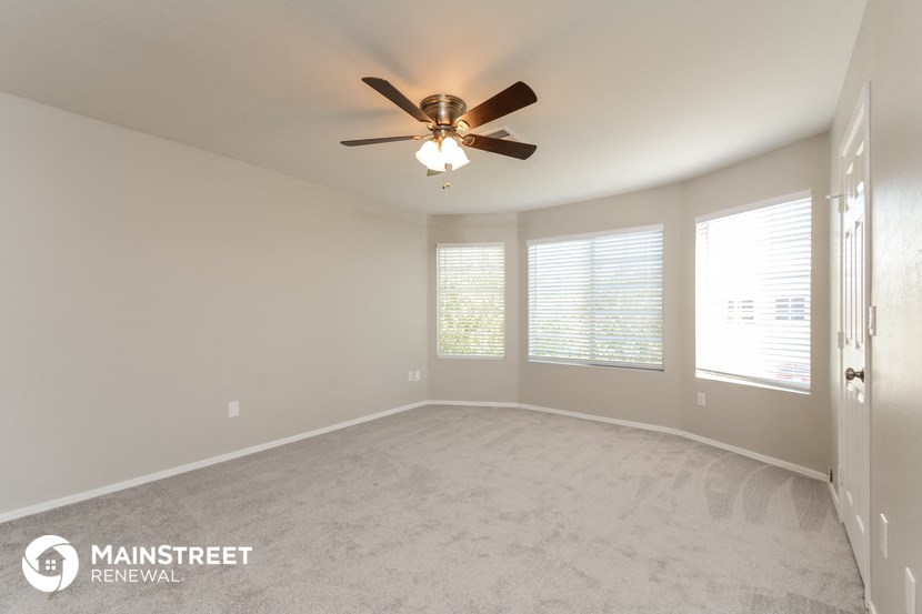 an empty living room with a ceiling fan and three windows