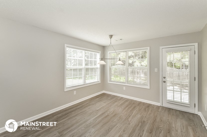 the living room of an apartment with wood flooring and windows