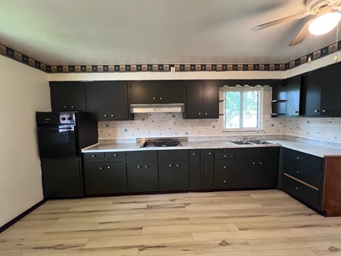 A kitchen with black cabinets and a wooden floor.