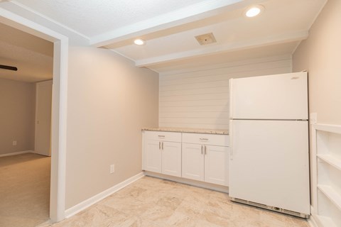 A white refrigerator is in a kitchen with white cabinets.