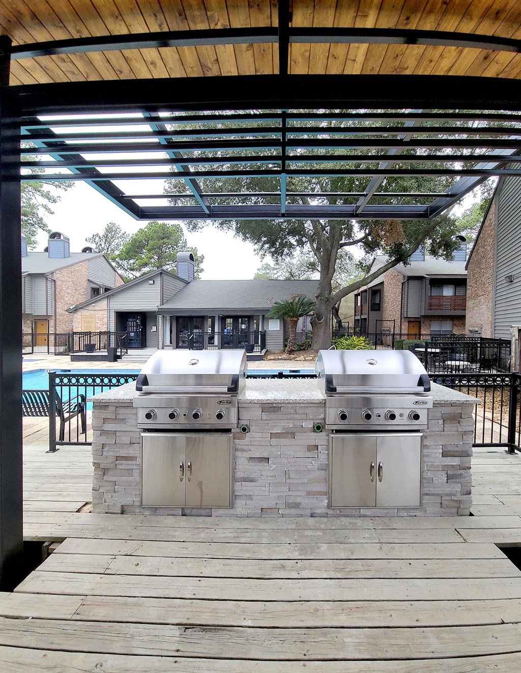 two stainless steel barbecue grills on a wooden deck next to a pool