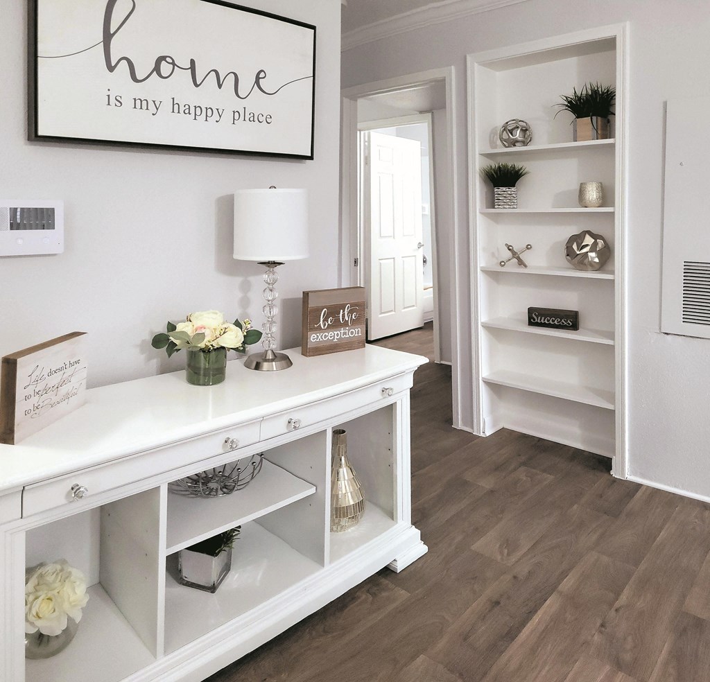 a living room with white shelves and a white table with a lamp