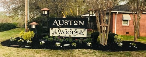A sign that says "Auston Woods" is in front of a house.
