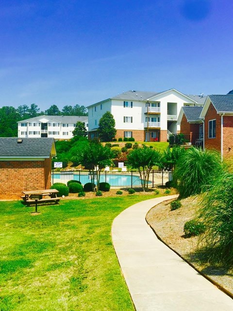 A grassy area with a bench and a pool in front of apartment buildings.