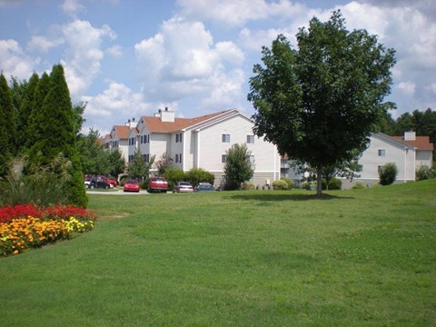 A white house with a red roof is surrounded by a green lawn and trees.