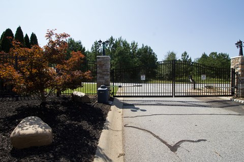 A black metal gate with a stone pillar and a tree with orange leaves in front of it.