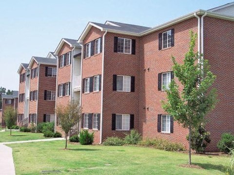 A red brick apartment building with green trees in front.