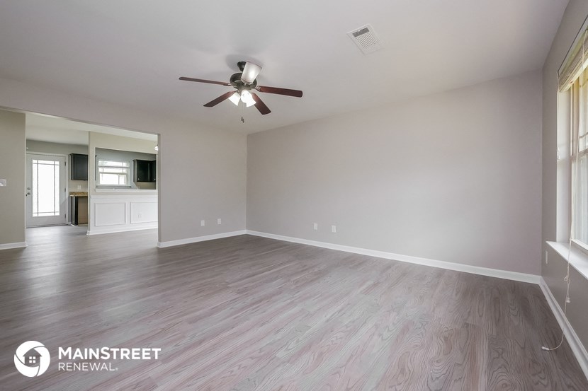 the spacious living room with wood flooring and a ceiling fan