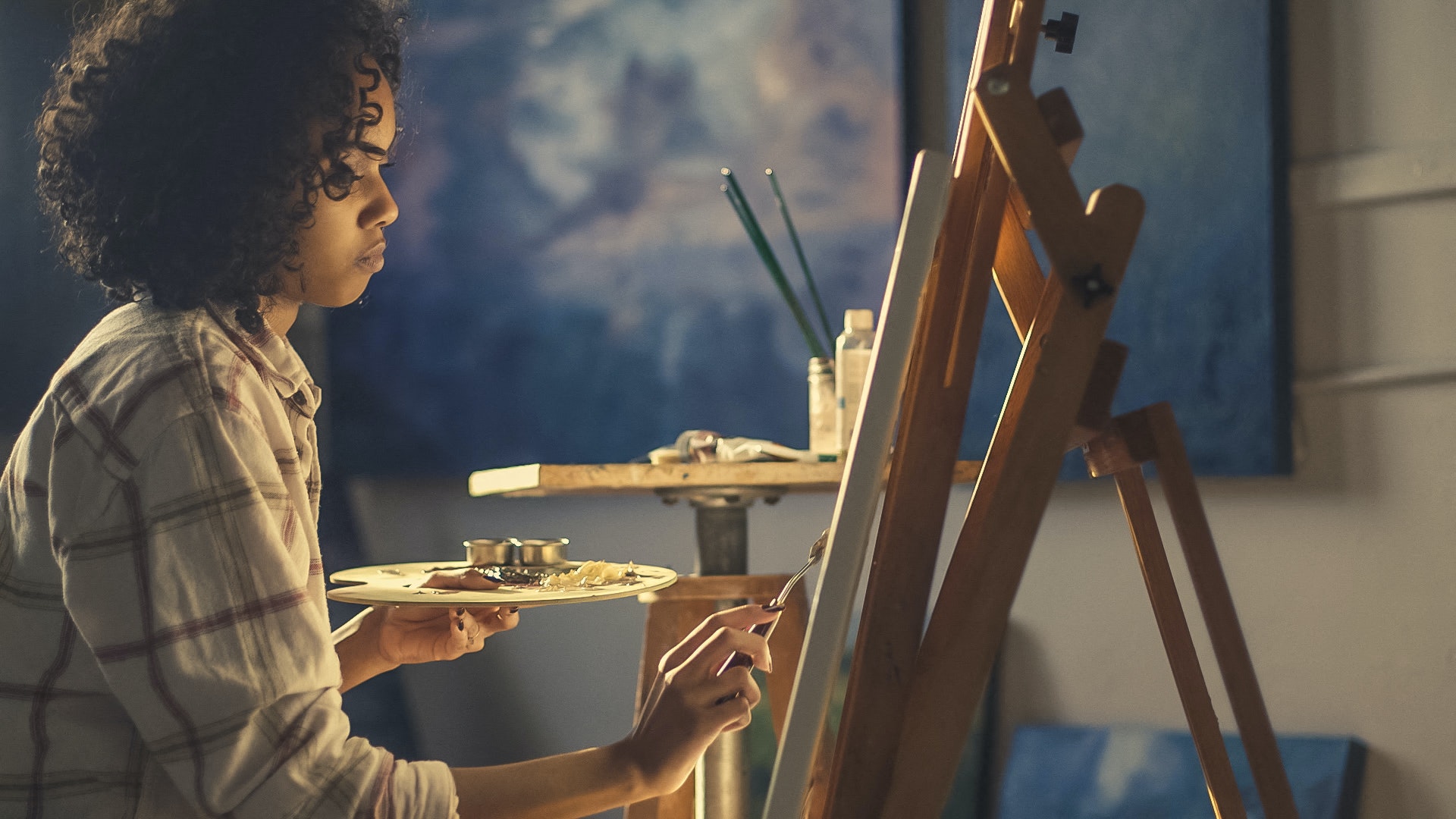 a woman painting at an easel with a plate of food in front of her