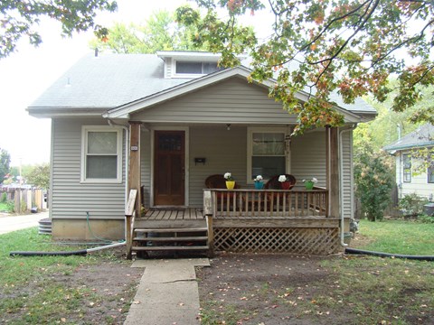 A small house with a porch and a hose on the ground.