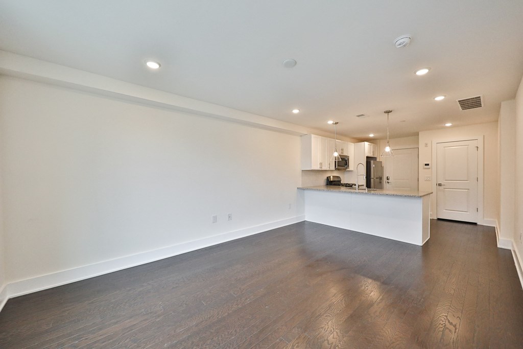 an empty living room and kitchen with white walls and wood flooring