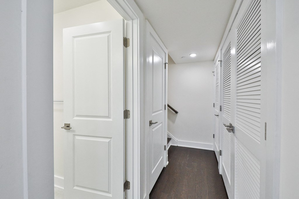 a hallway with white closets and doors and a wood floor