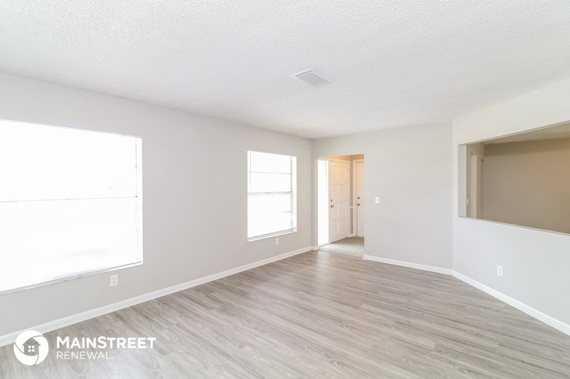 the living room of an apartment with wood flooring and white walls