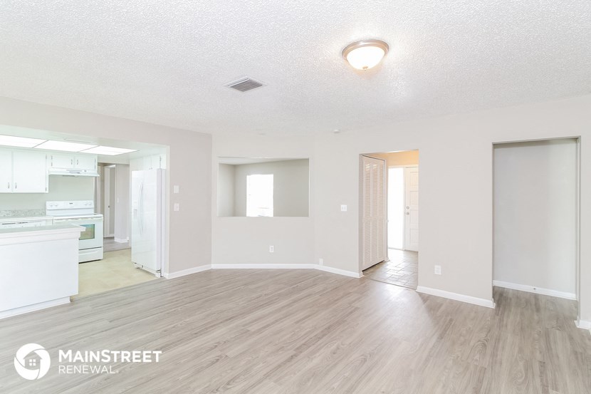 a spacious living room and kitchen with white walls and wood flooring