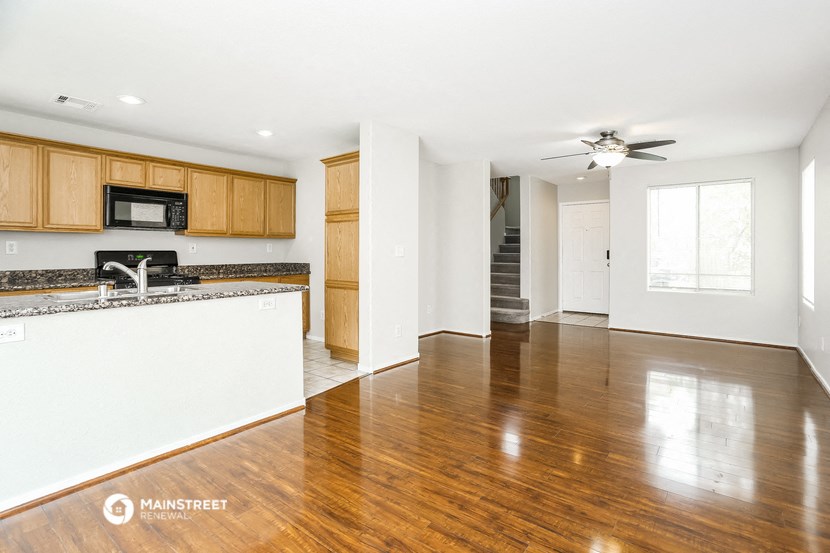 an empty living room and kitchen with wood flooring and white walls