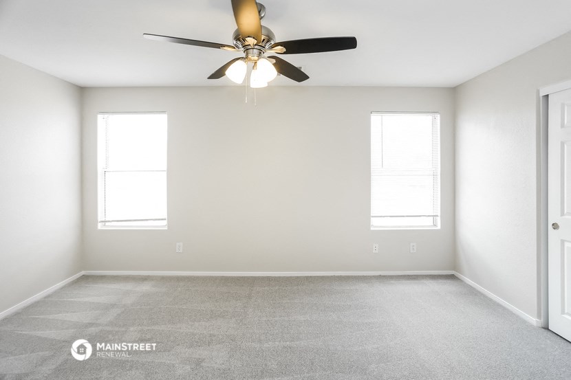 an empty room with a ceiling fan and two windows